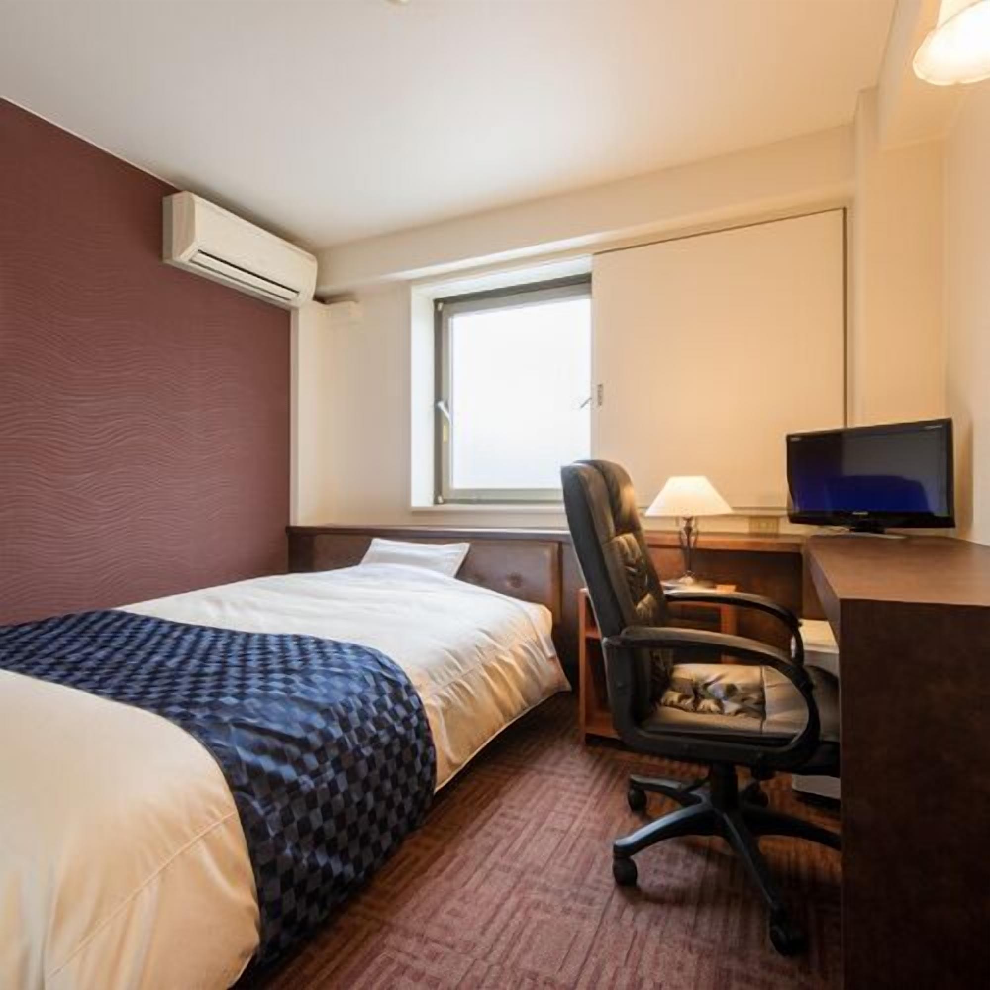 Una habitación de hotel con una cama, un escritorio con silla, un televisor y un equipo de aire acondicionado.