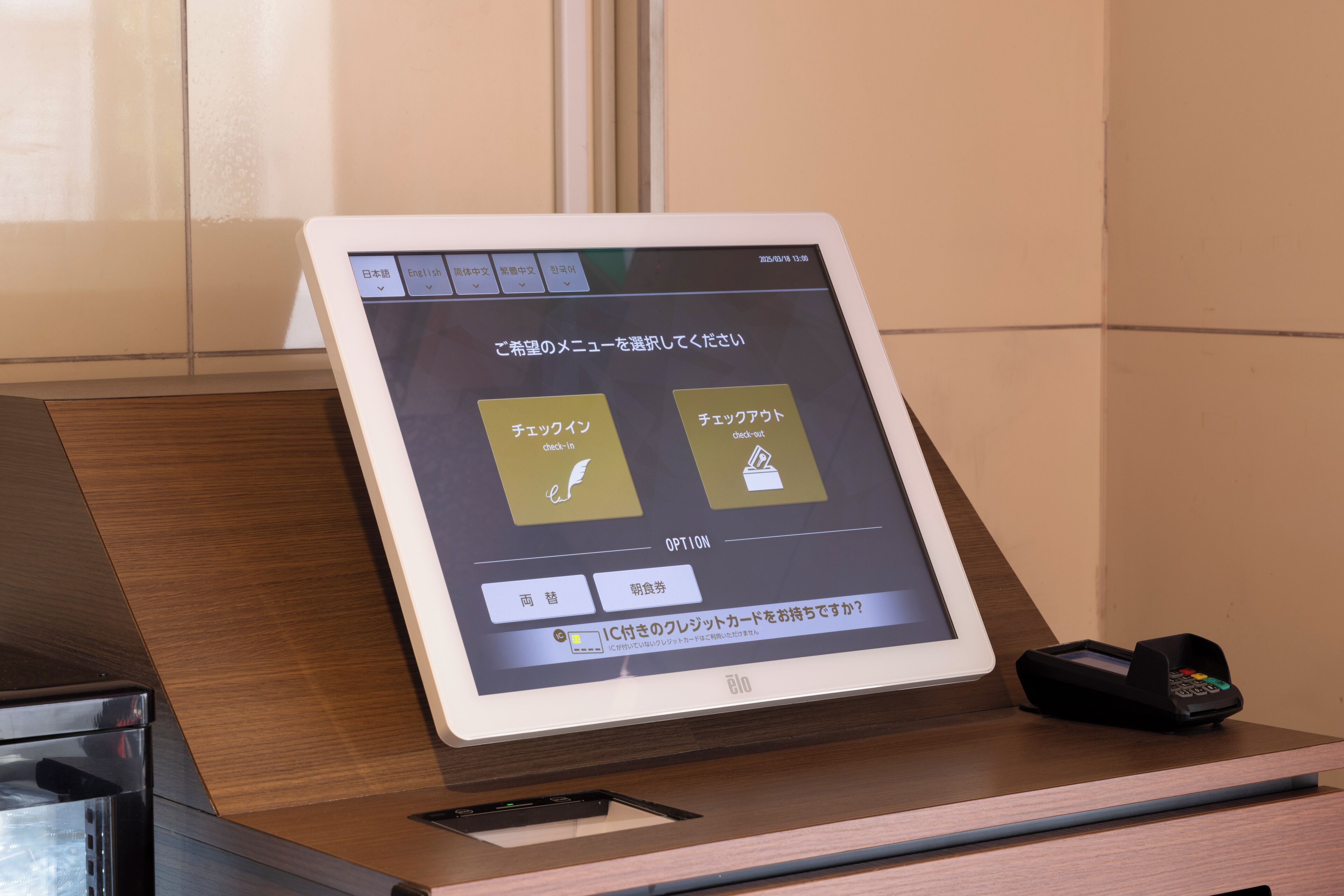 Un quiosco digital con pantalla que muestra opciones en japonés, un terminal de pago y un cargador para teléfonos móviles.