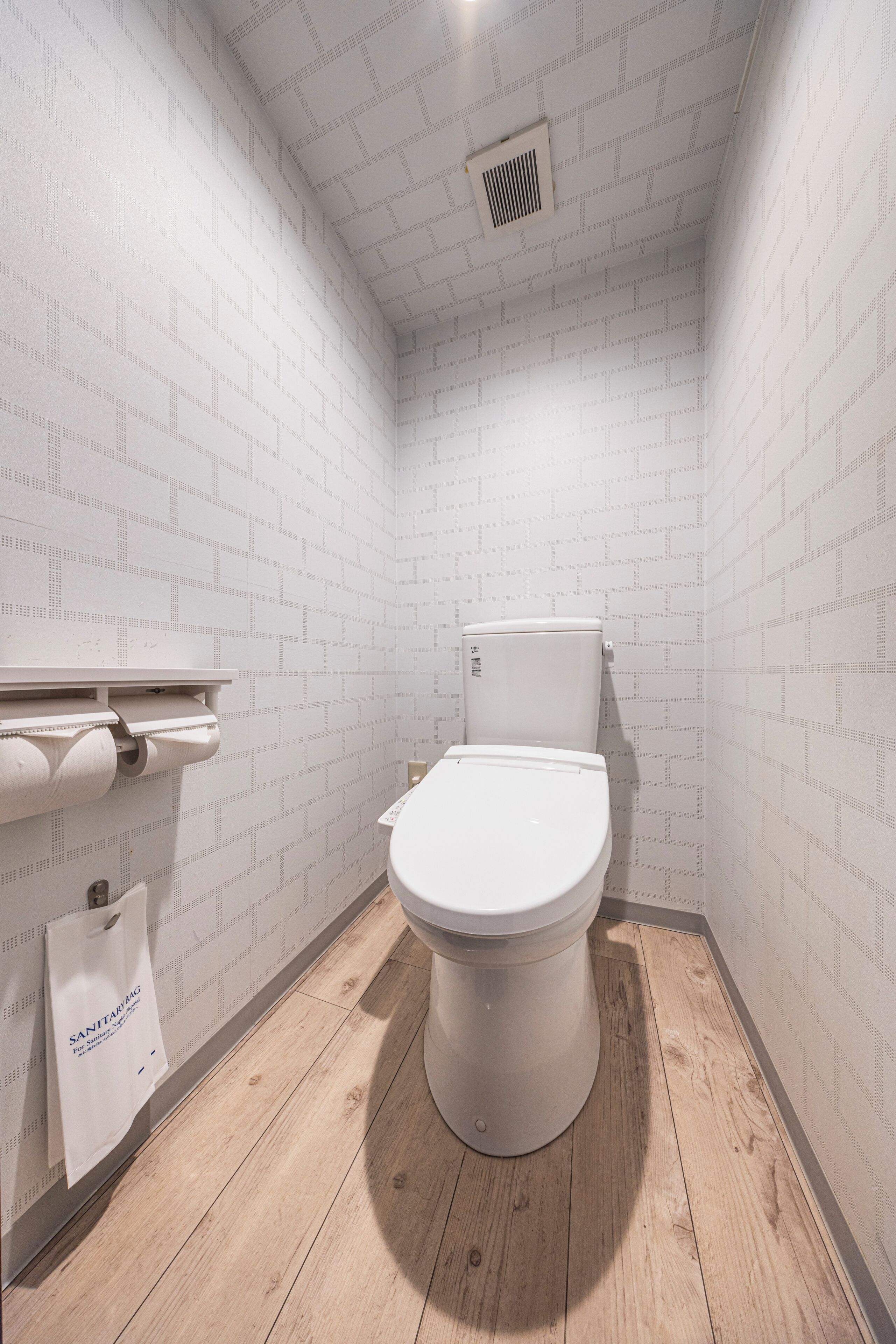 A small, clean bathroom with a white toilet, a toilet paper holder, and a wooden floor.