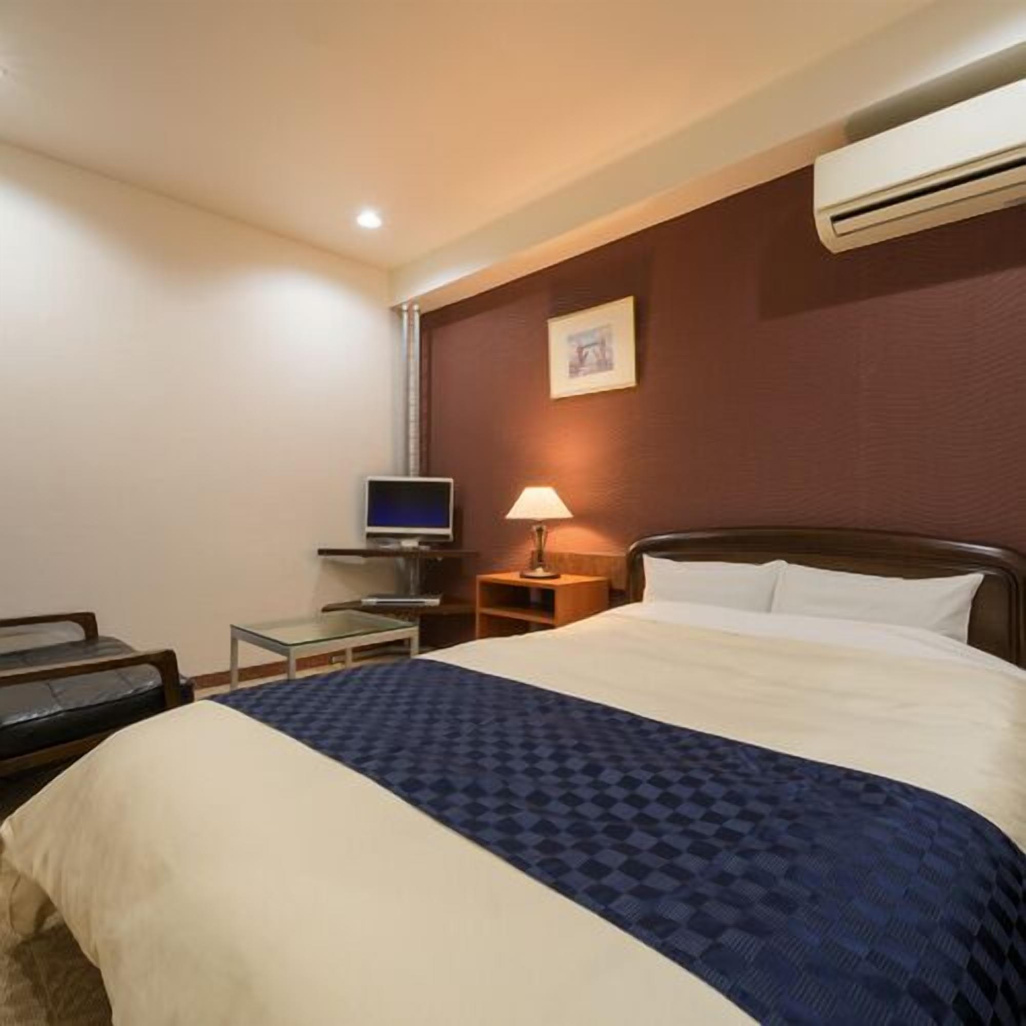 Una habitación de hotel con una cama, televisión, escritorio y lámpara.