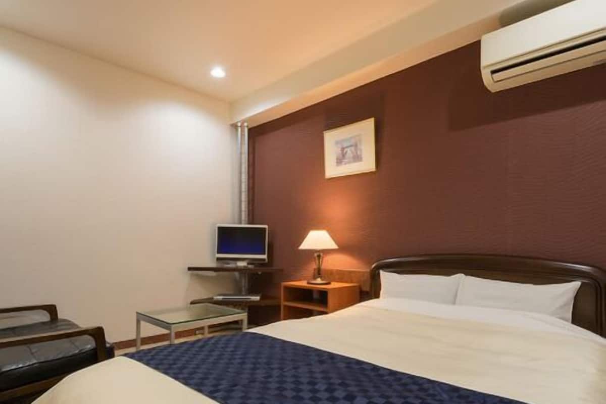 Una habitación de hotel con una cama, televisión, escritorio y lámpara.