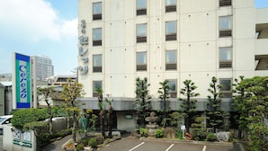 Un hotel de varios pisos con fachada moderna, un letrero llamativo y una entrada ajardinada con diversas plantas y un jardín de rocas.