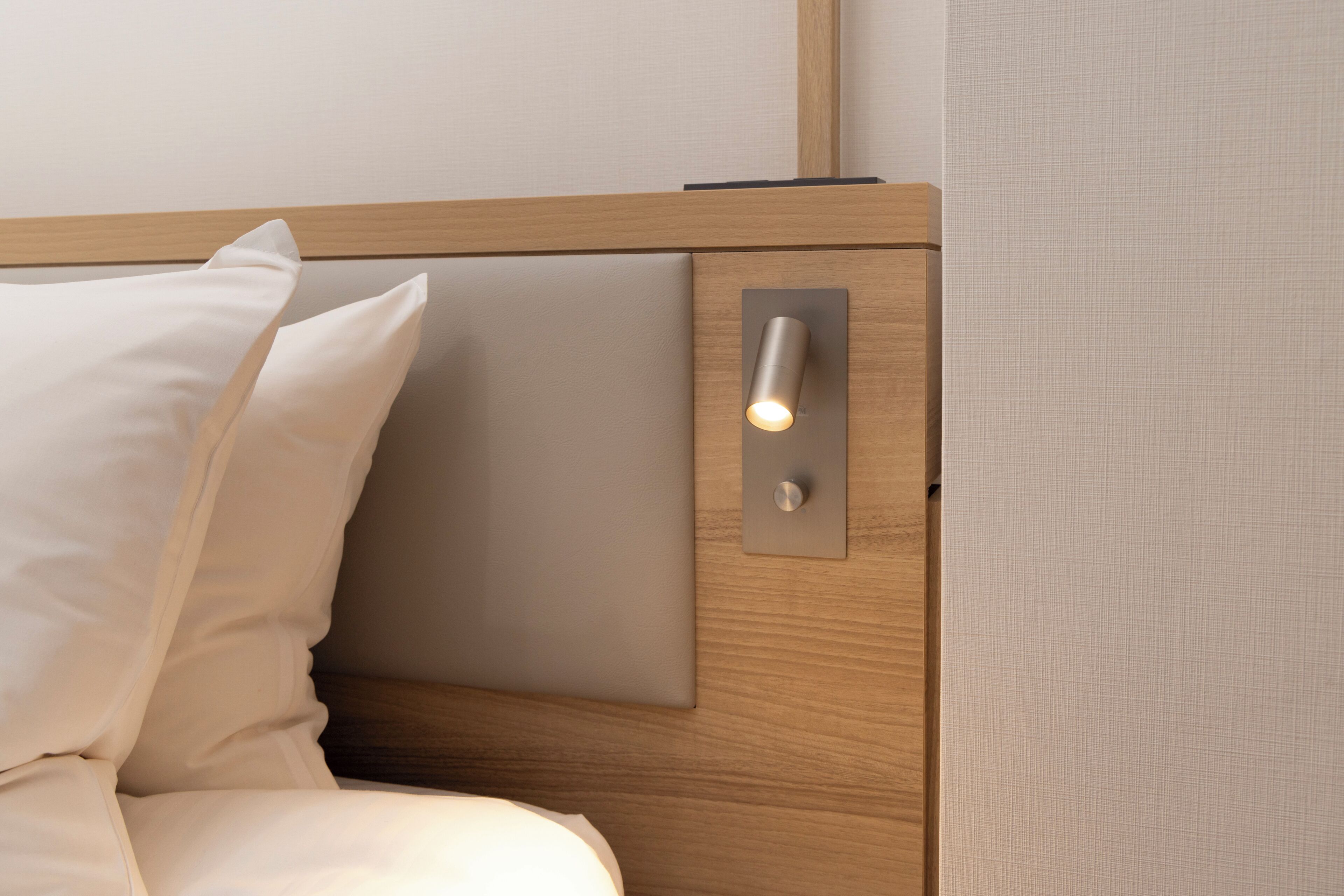 A bed with a wooden headboard, a bedside table, and a wall-mounted light fixture.