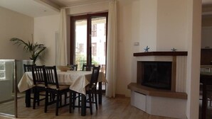 A dining area with a table set for four, a fireplace, and a view through a window. - S083 - Sirolo, new five-room apartment with garden (Sirolo)