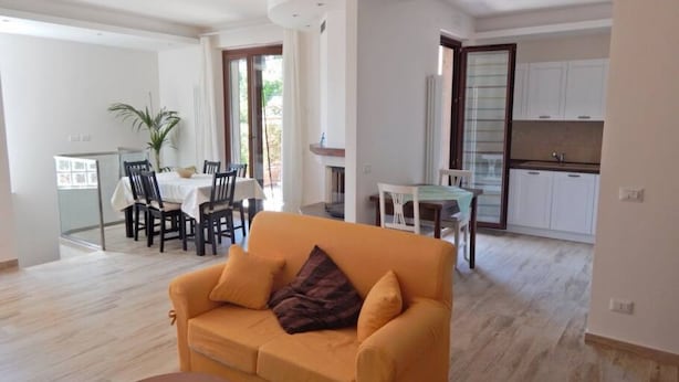 A living room with a sofa, a dining area with chairs and a table, and a kitchen area with cabinets. - S083 - Sirolo, new five-room apartment with garden (Sirolo)
