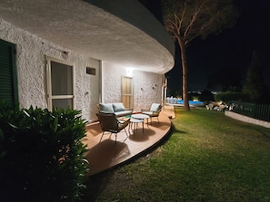 Une terrasse avec des meubles d’extérieur, une piscine et un bâtiment blanc à la texture particulière.