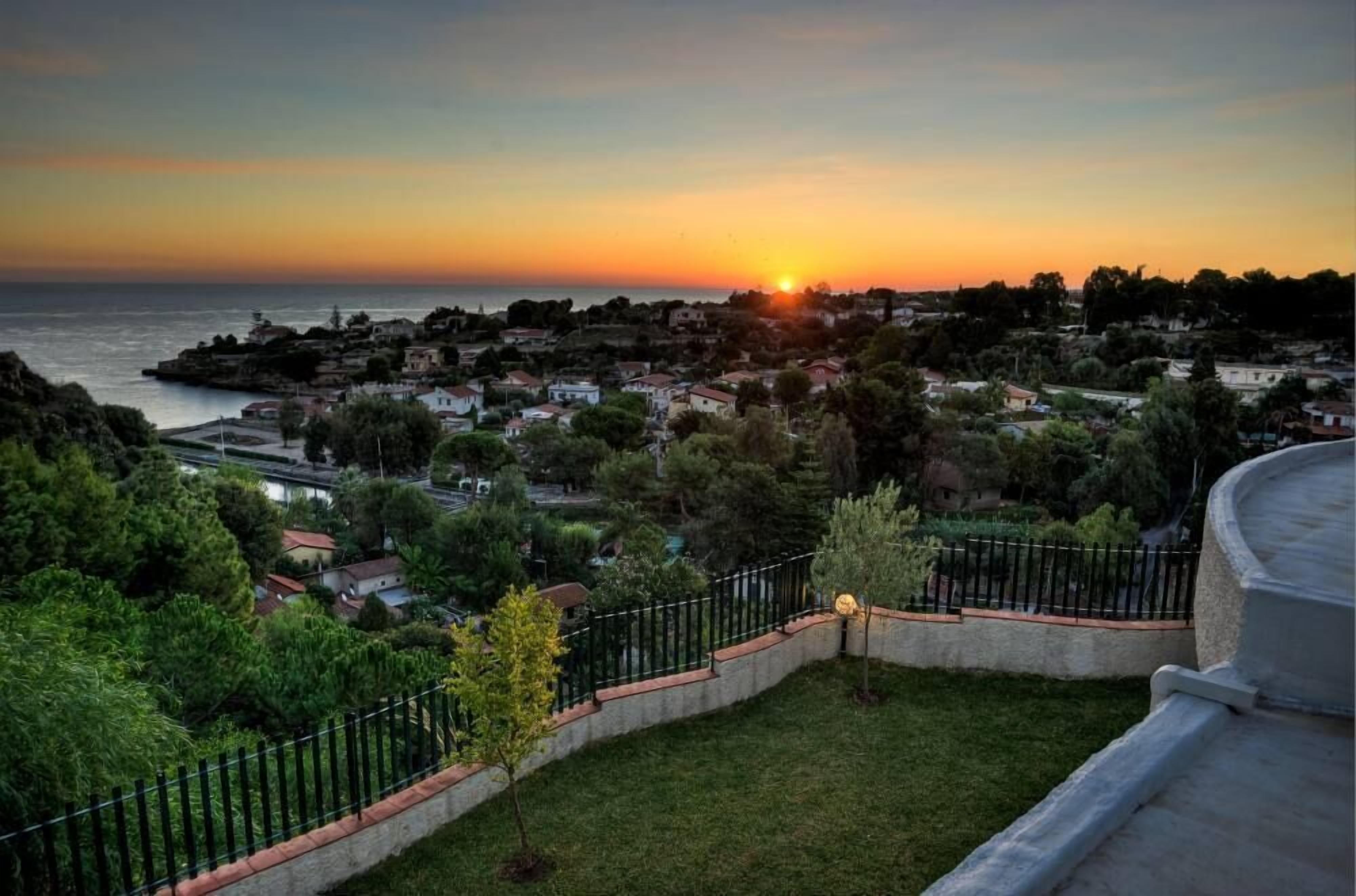 Eine Küstenstadt im Abendlicht mit Häusern, viel Grün und Blick auf das Meer.