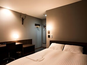 Una habitación de hotel con una cama, mesitas de noche, un escritorio y un espejo.