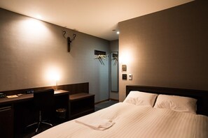 Una habitación de hotel con cama, escritorio, silla y perchero.