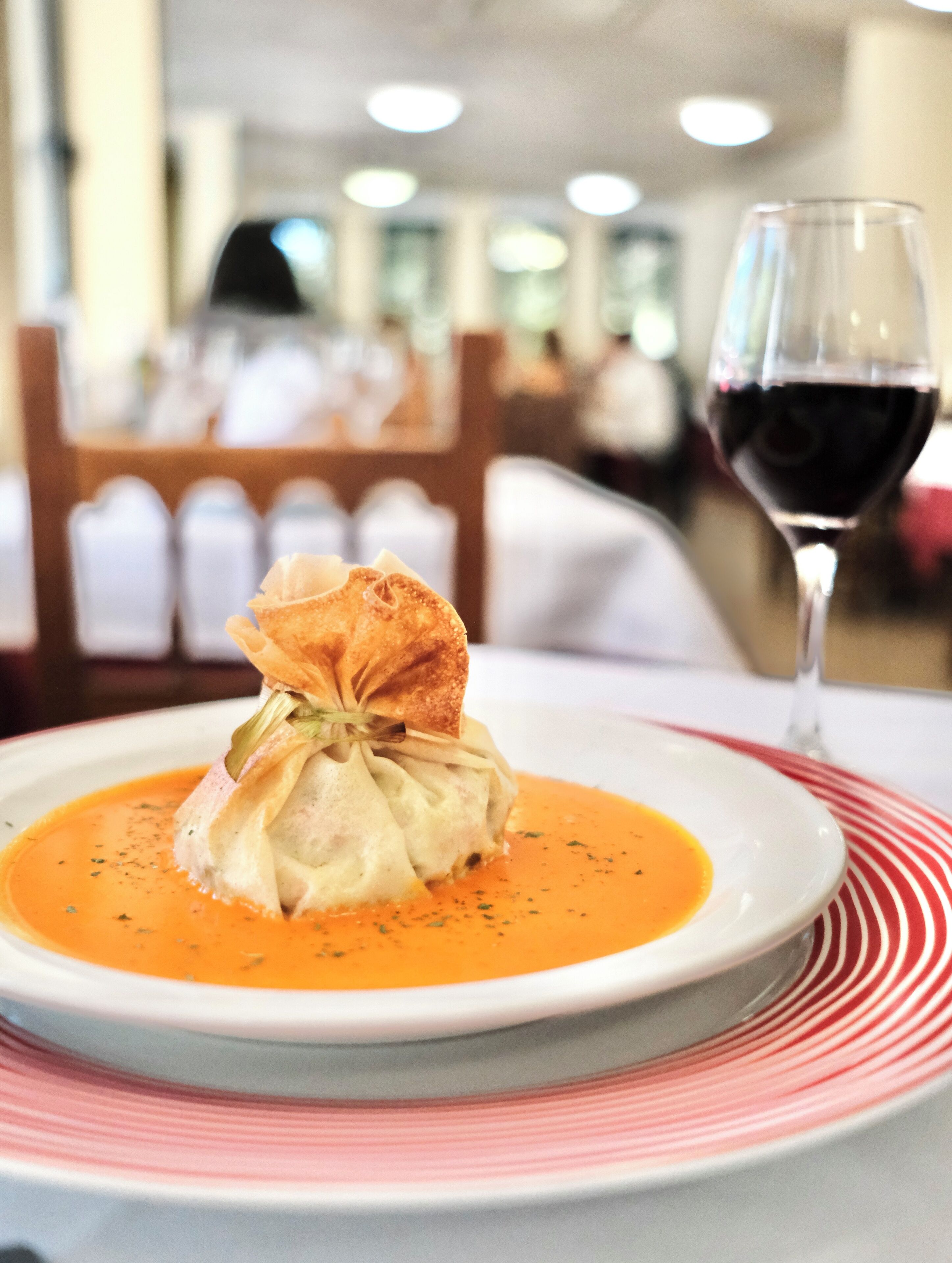 Un plato de comida con sopa y una copa de vino tinto sobre una mesa.