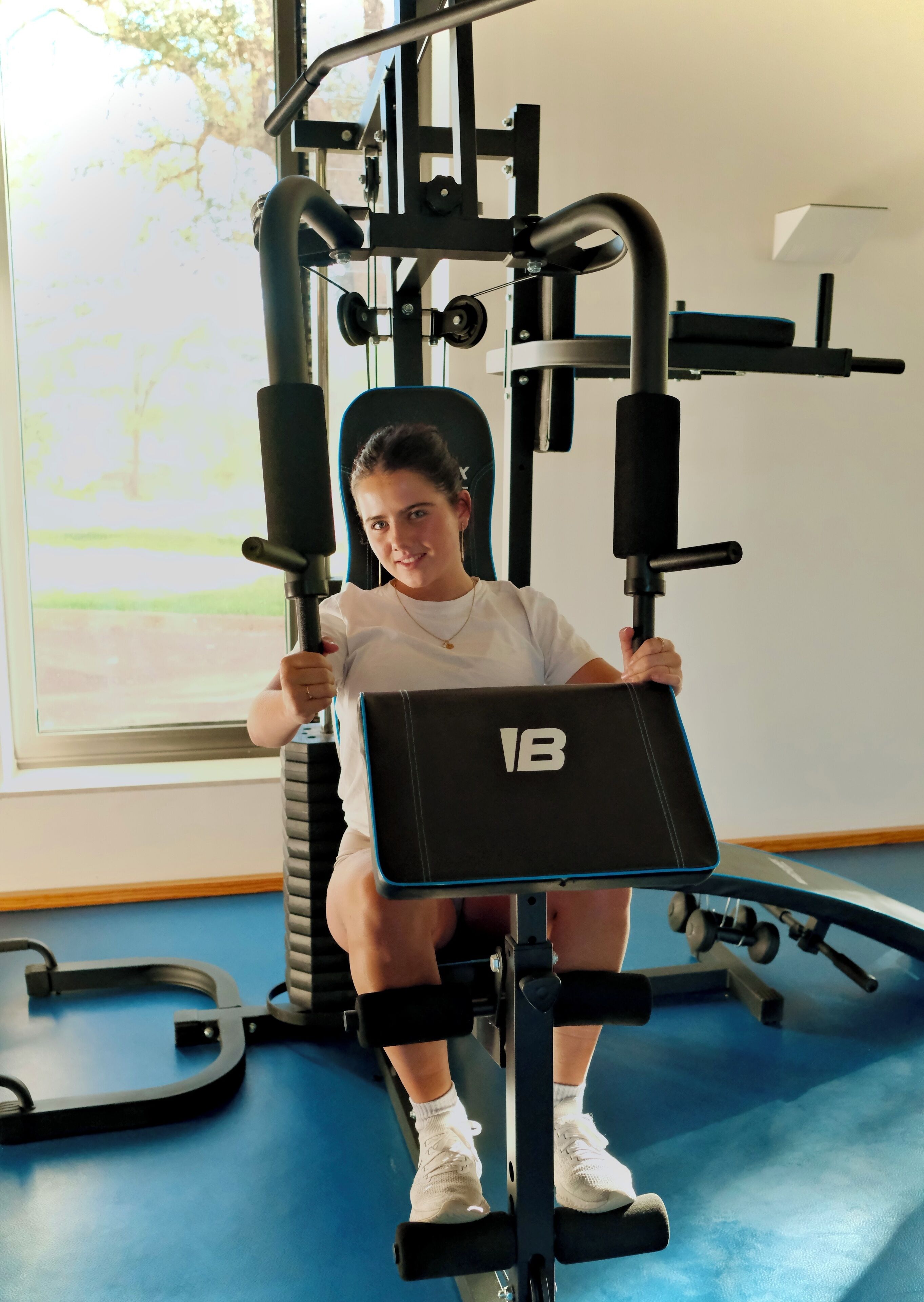 Una persona usando una máquina para piernas en un gimnasio con un ventanal grande al fondo.