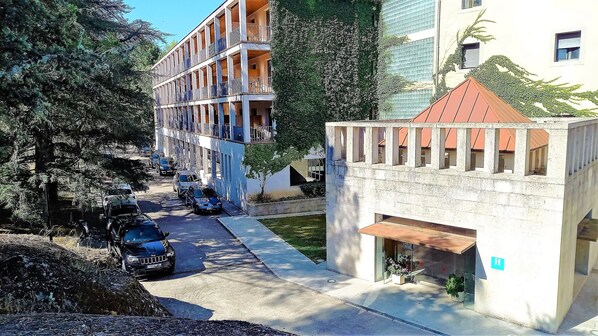 A multi-story building with balconies, a parking area, and a small garden. - Balneario de Retortillo (Retortillo)