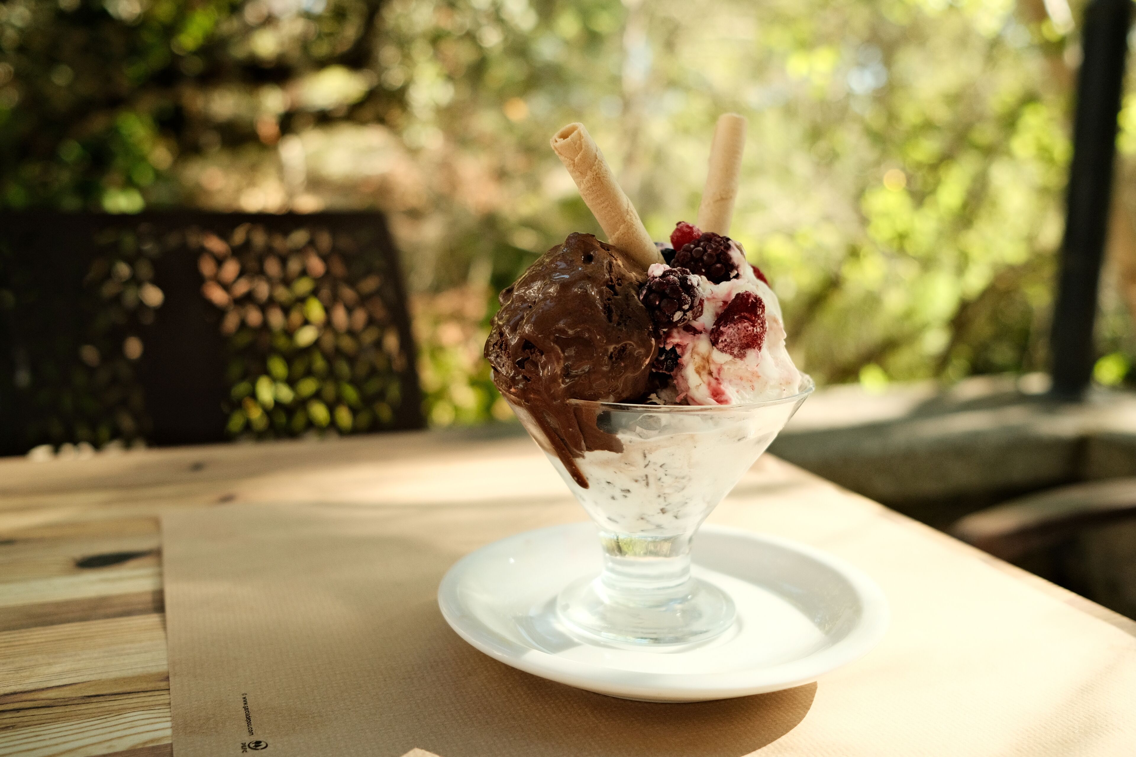 A dessert in a glass bowl on a white plate, with a blurred outdoor background.