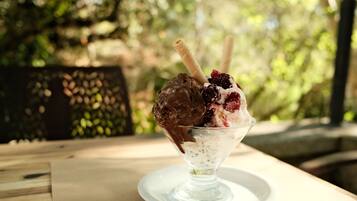 Un postre en un bol de vidrio sobre un plato blanco, con un fondo desenfocado al aire libre.