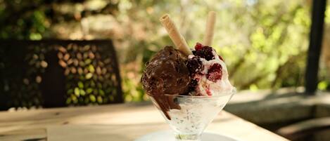 A dessert in a glass bowl on a white plate, with a blurred outdoor background.