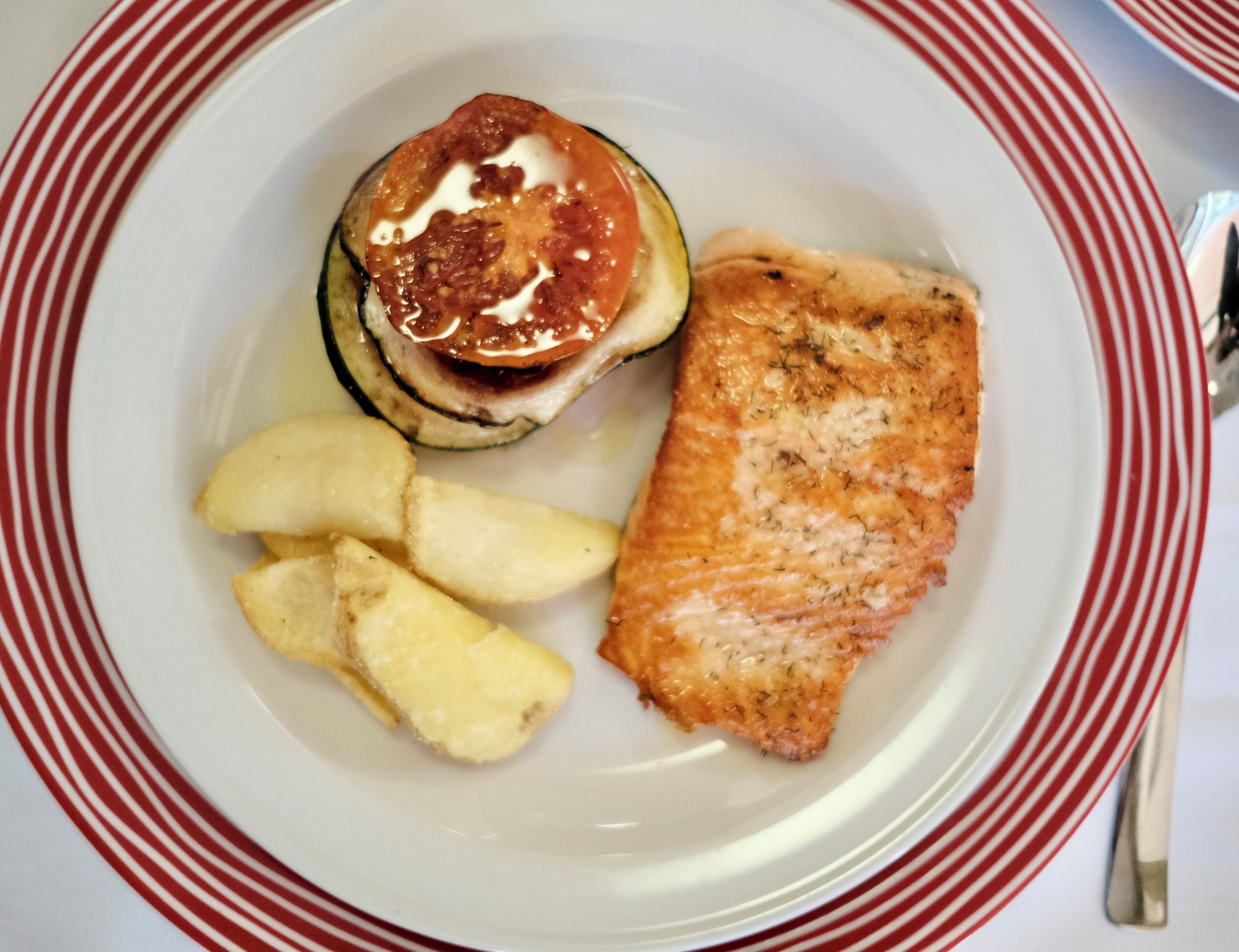 Un plato con un trozo de salmón, una rodaja de tomate y algunas patatas fritas.