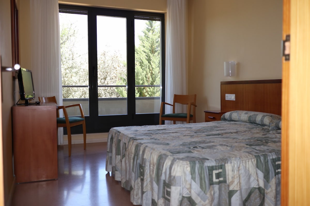 A hotel room with a bed, two chairs, a desk, and a window with curtains.