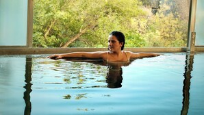 Una persona en una piscina con vistas a árboles y rocas a través de amplios ventanales.