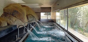 A spa area with a hot tub, stone wall, and a view of trees through large windows. - Balneario de Retortillo (Retortillo)