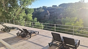 Terraza con sillones de descanso y barandilla, con vistas a una zona boscosa y acantilados rocosos.