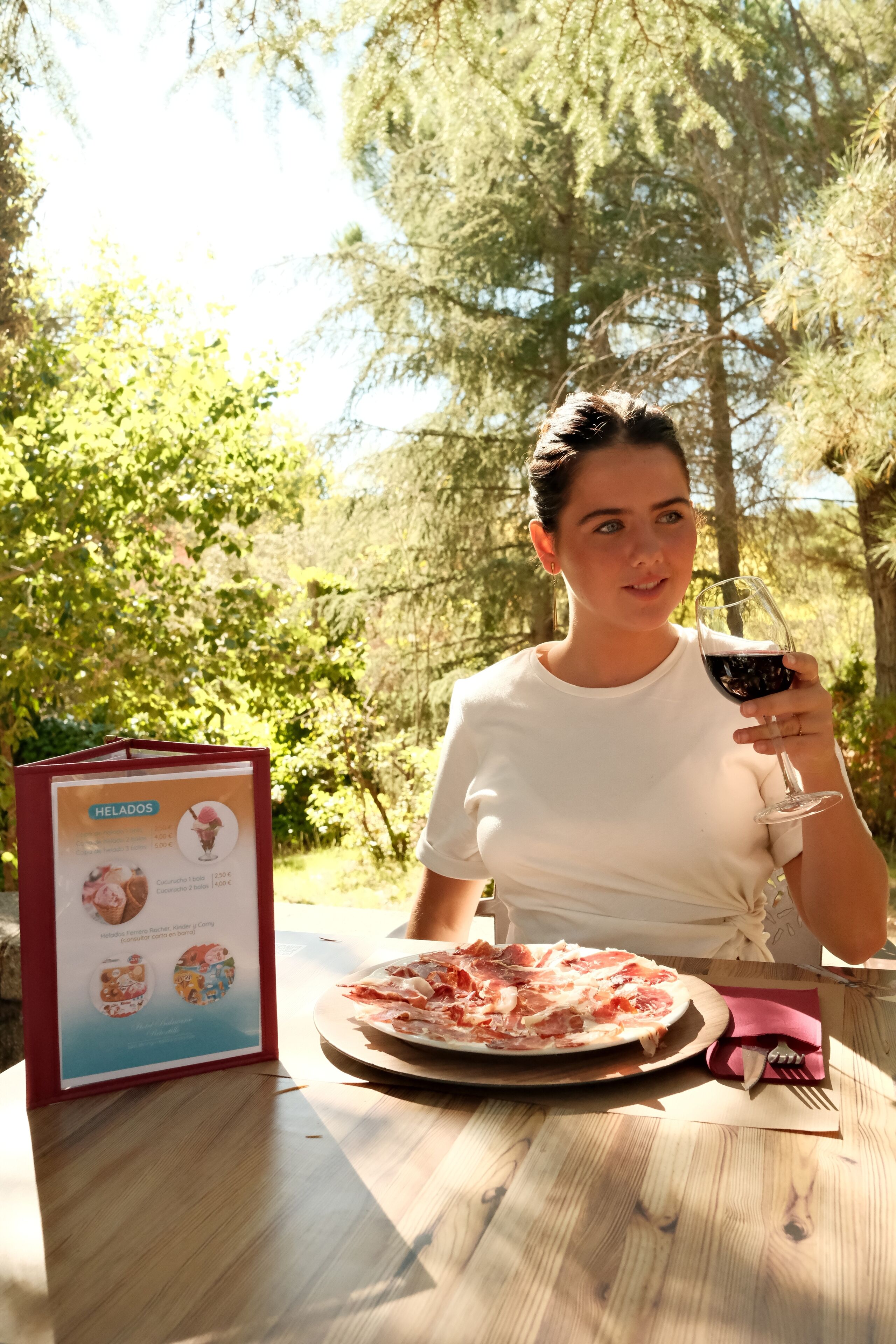 A person sitting at a table with a menu and a plate of food, holding a glass of red wine.