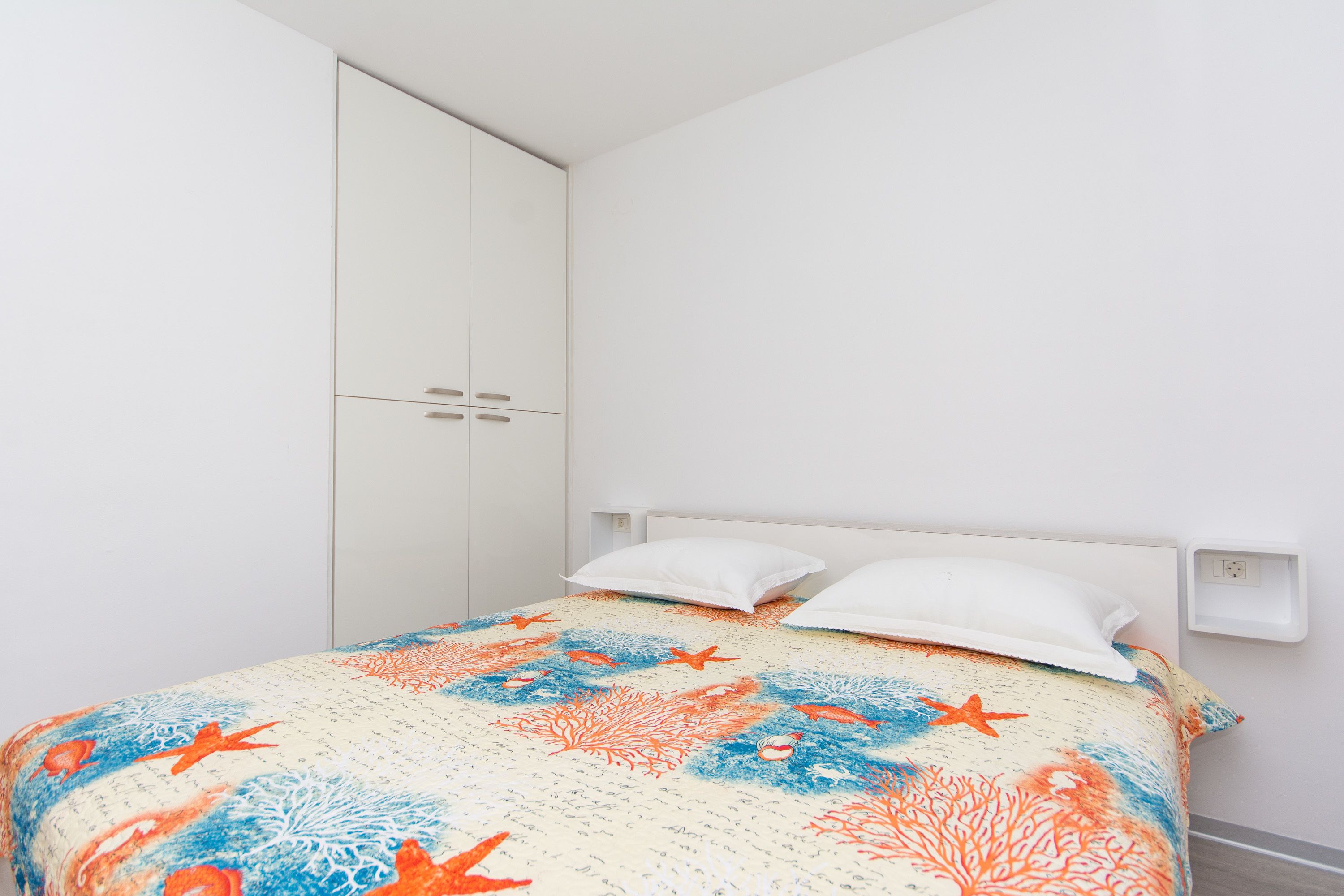 Un dormitorio con cama, paredes blancas, un armario blanco y cabecero blanco.
