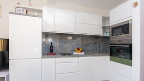 Una cocina moderna con armarios blancos, salpicadero de mármol, horno empotrado y una radio en la encimera.