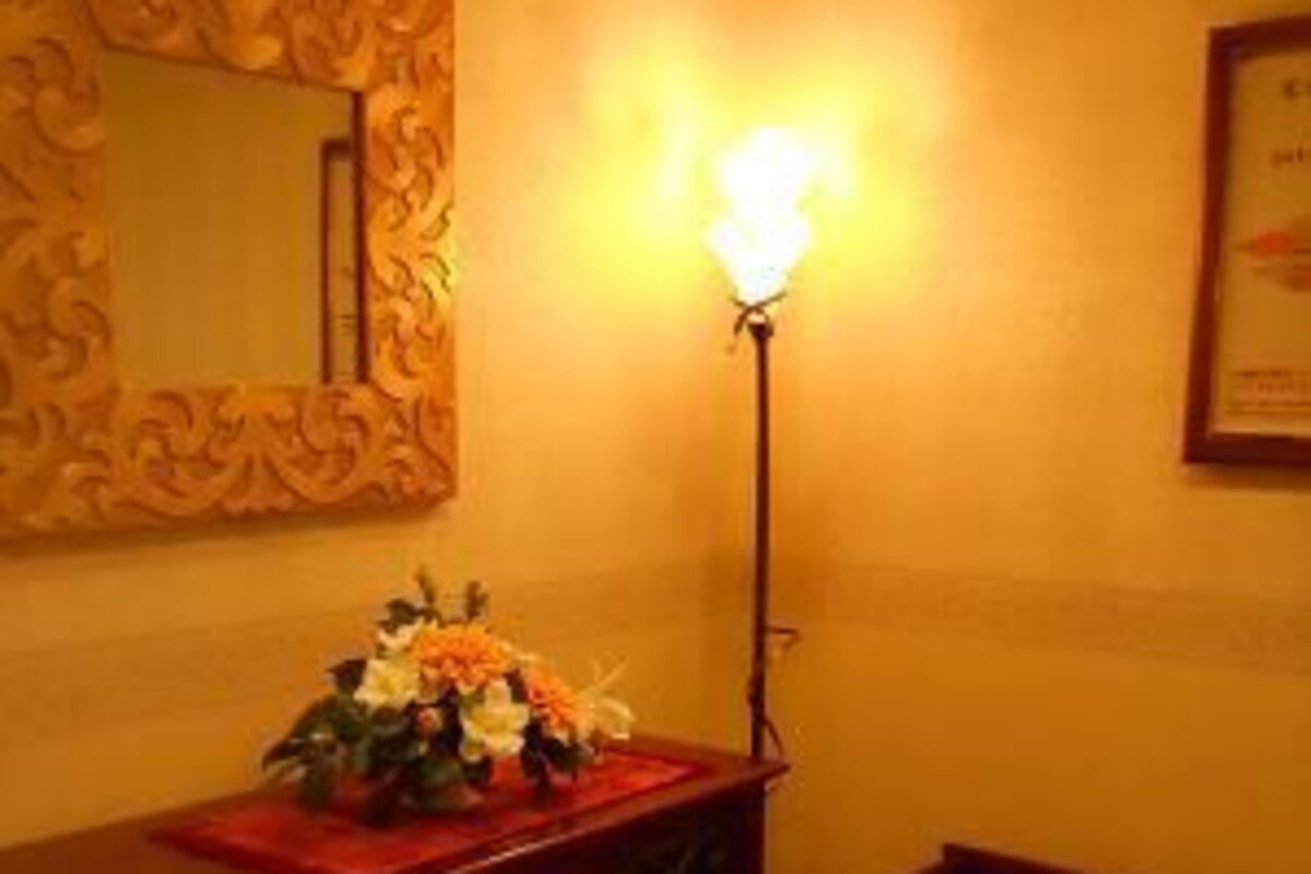 Una habitación con un aparador de madera, una lámpara, una silla y un espejo en la pared.