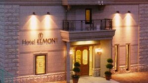 A hotel entrance with a sign reading 'Hotel ELMONT,' a balcony with a railing, and a door with a light fixture above it.