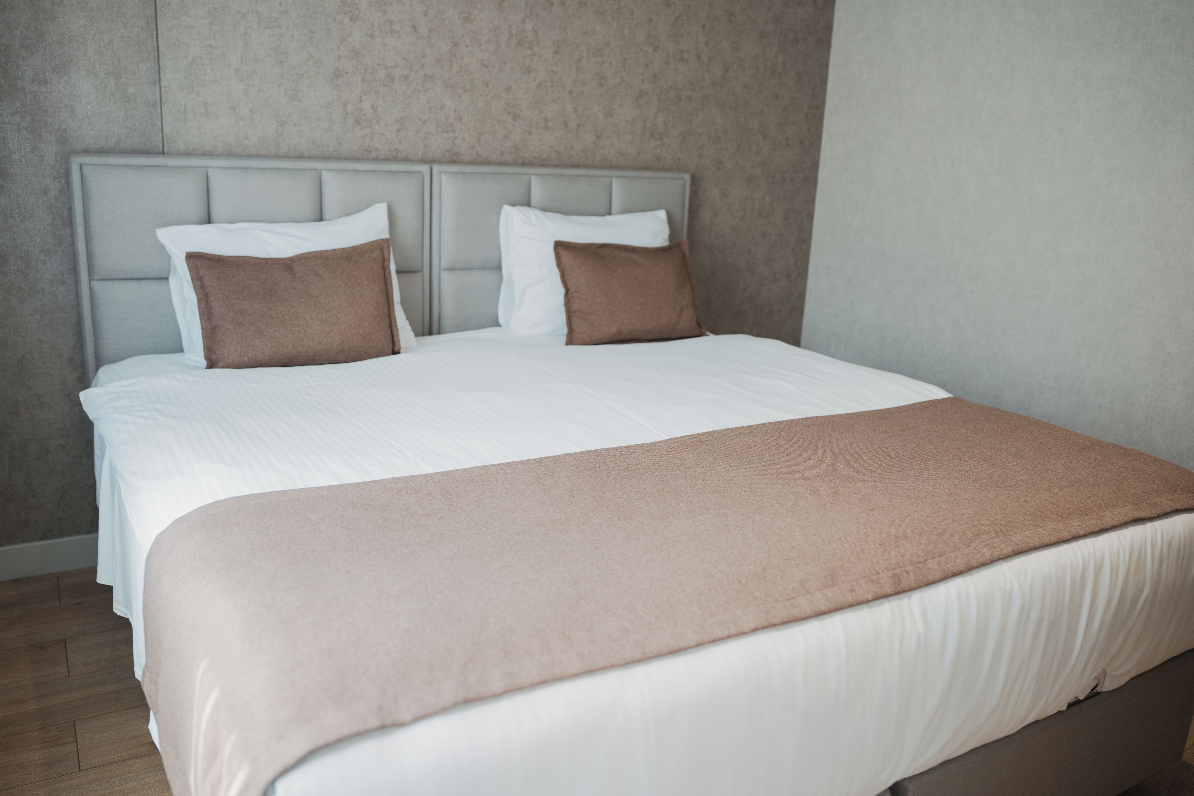 A bed with a white mattress, two pillows, and a brown throw blanket.