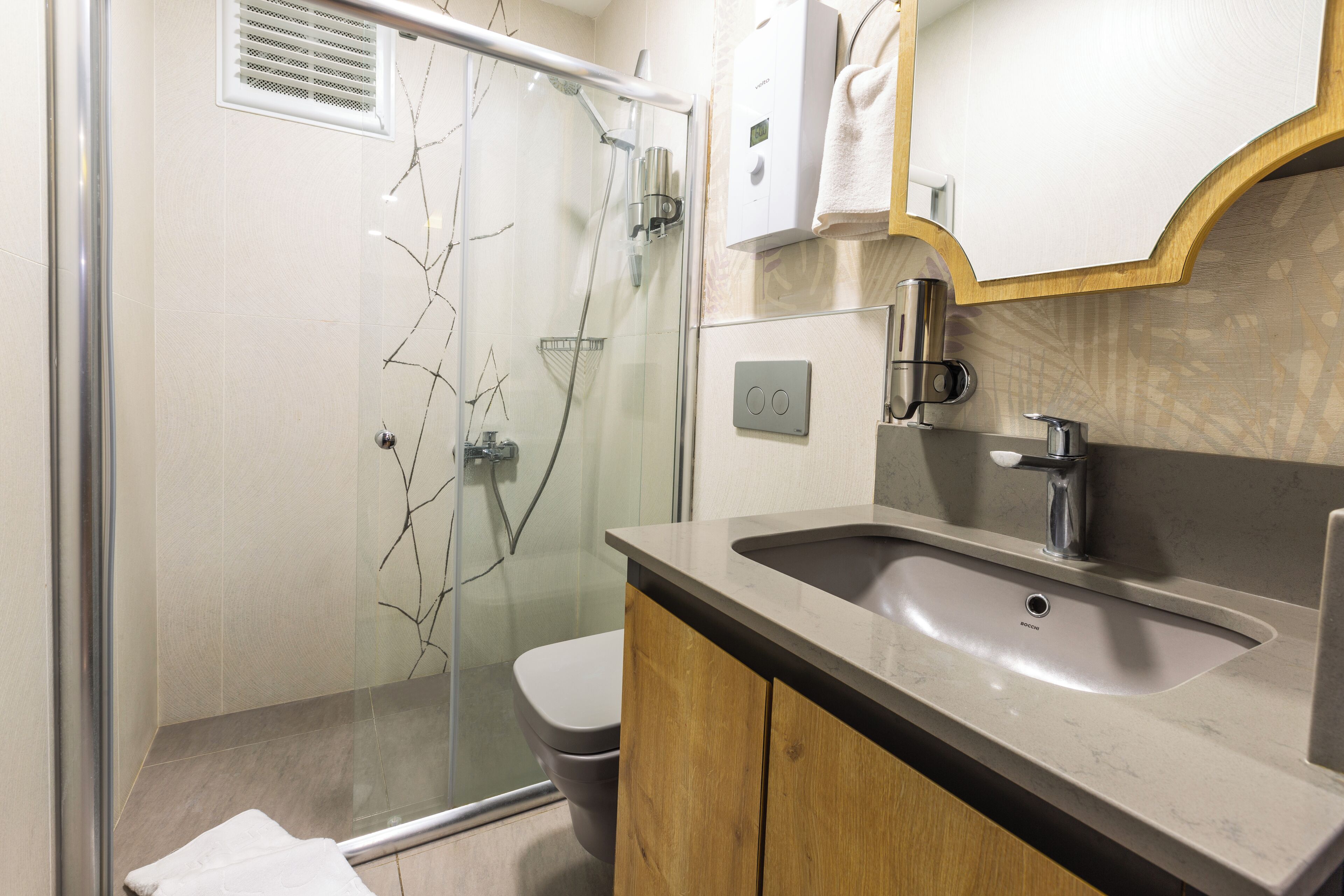 Un baño moderno con cabina de ducha de vidrio, un inodoro, un lavabo con gabinete de madera y una toalla colgada en la pared.