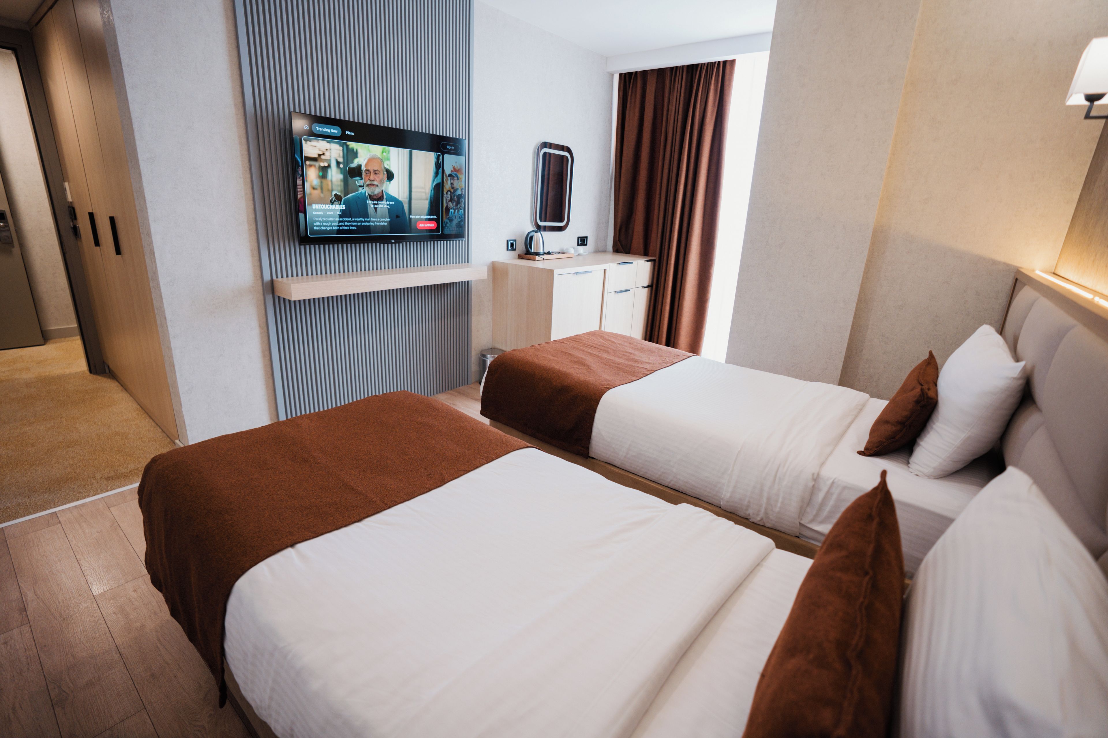 A hotel room with two beds, a television, a desk, and a mirror.