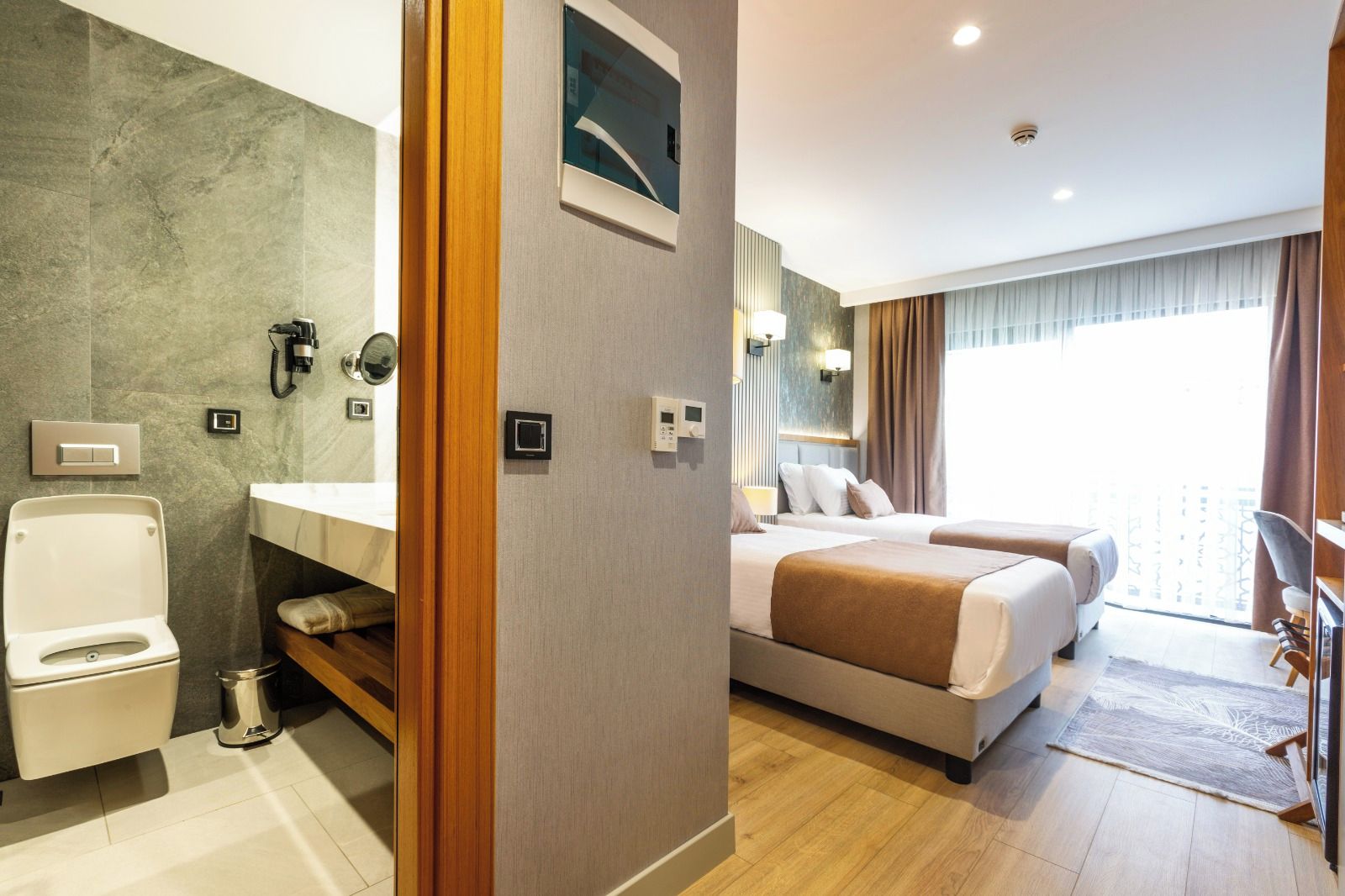 A hotel room with a bathroom, a bed, a bedside table, a lamp, and a window with curtains.