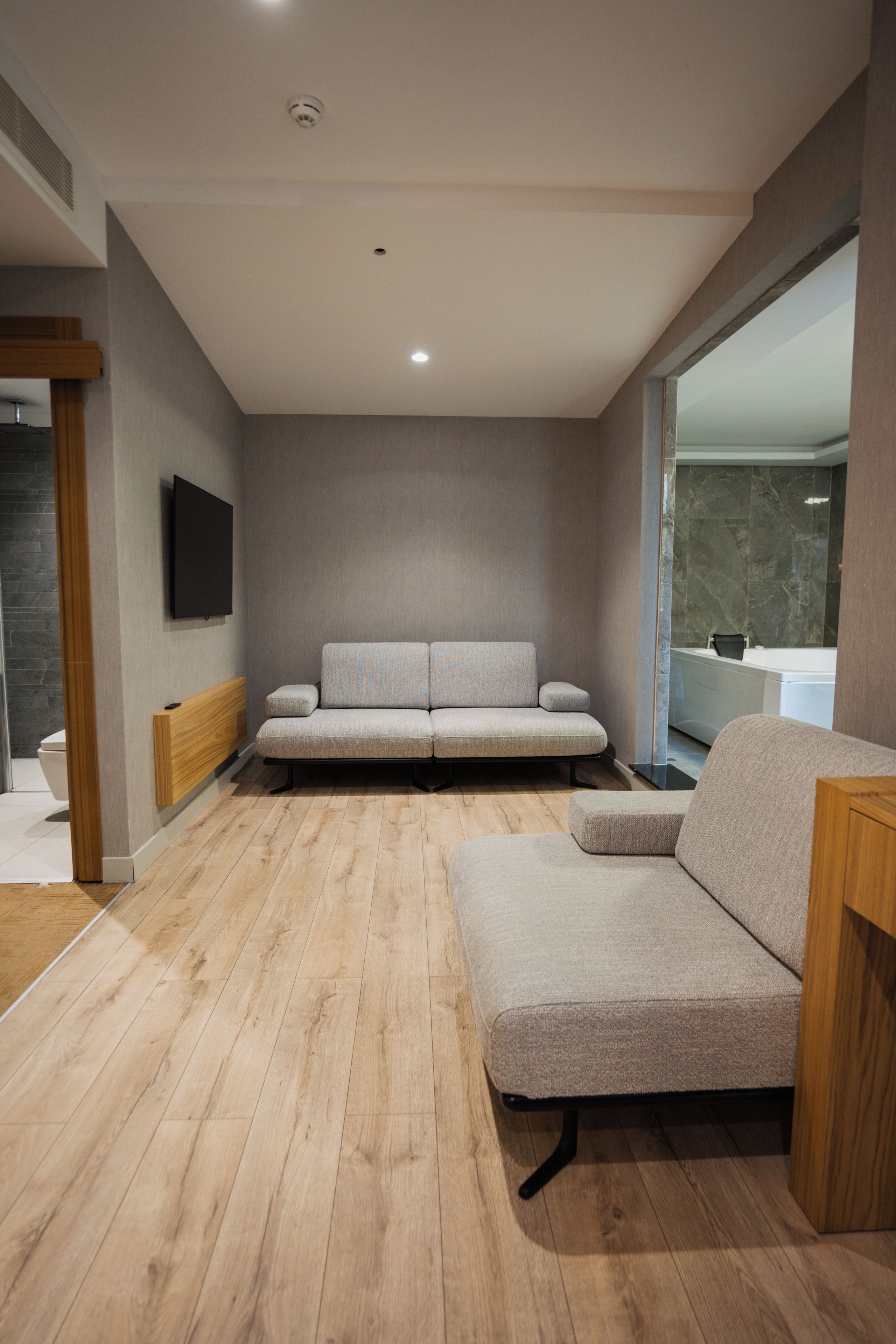 A modern living room with a sofa set, wooden flooring, and a television mounted on the wall.