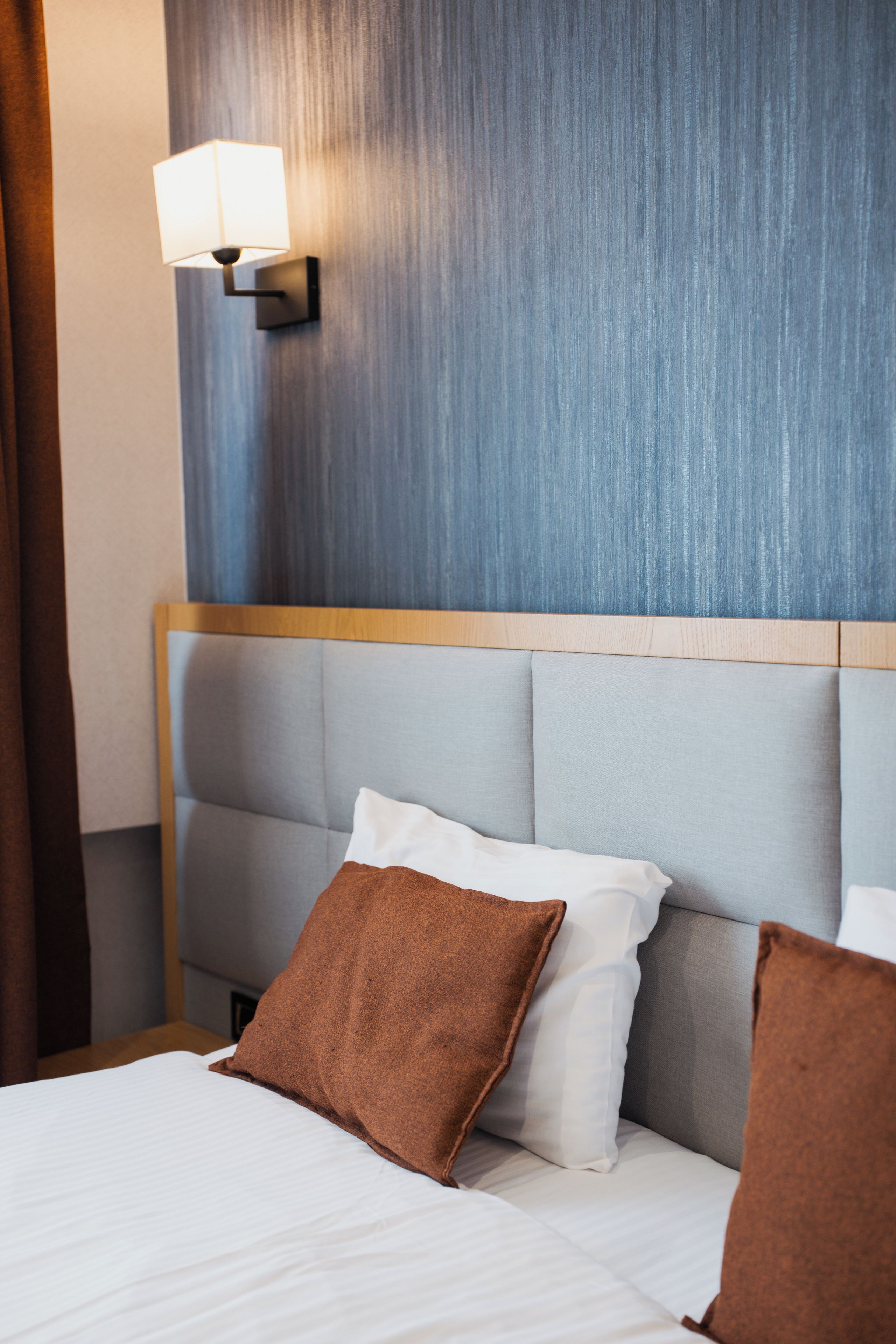 Una habitación de hotel con una cama, una lámpara de pared y un cabecero.