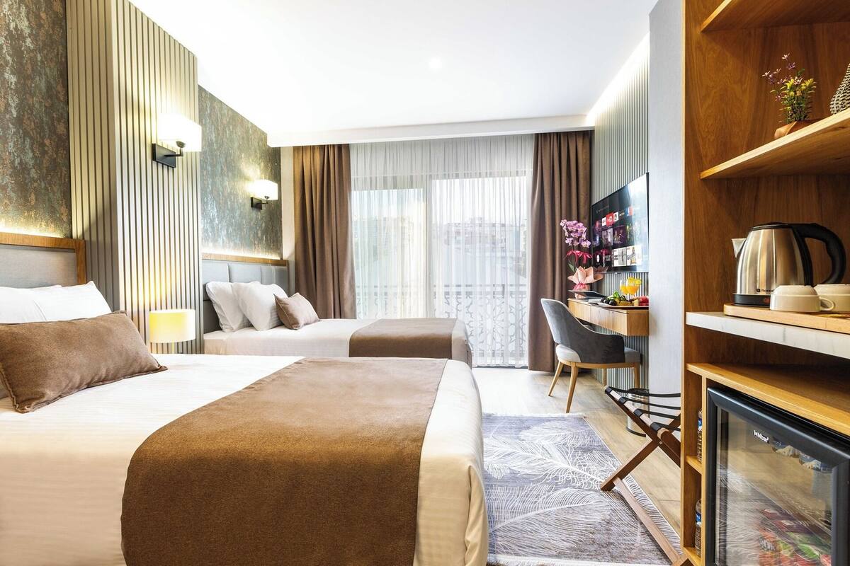 A hotel room with two beds, a desk, a television, and a minibar.