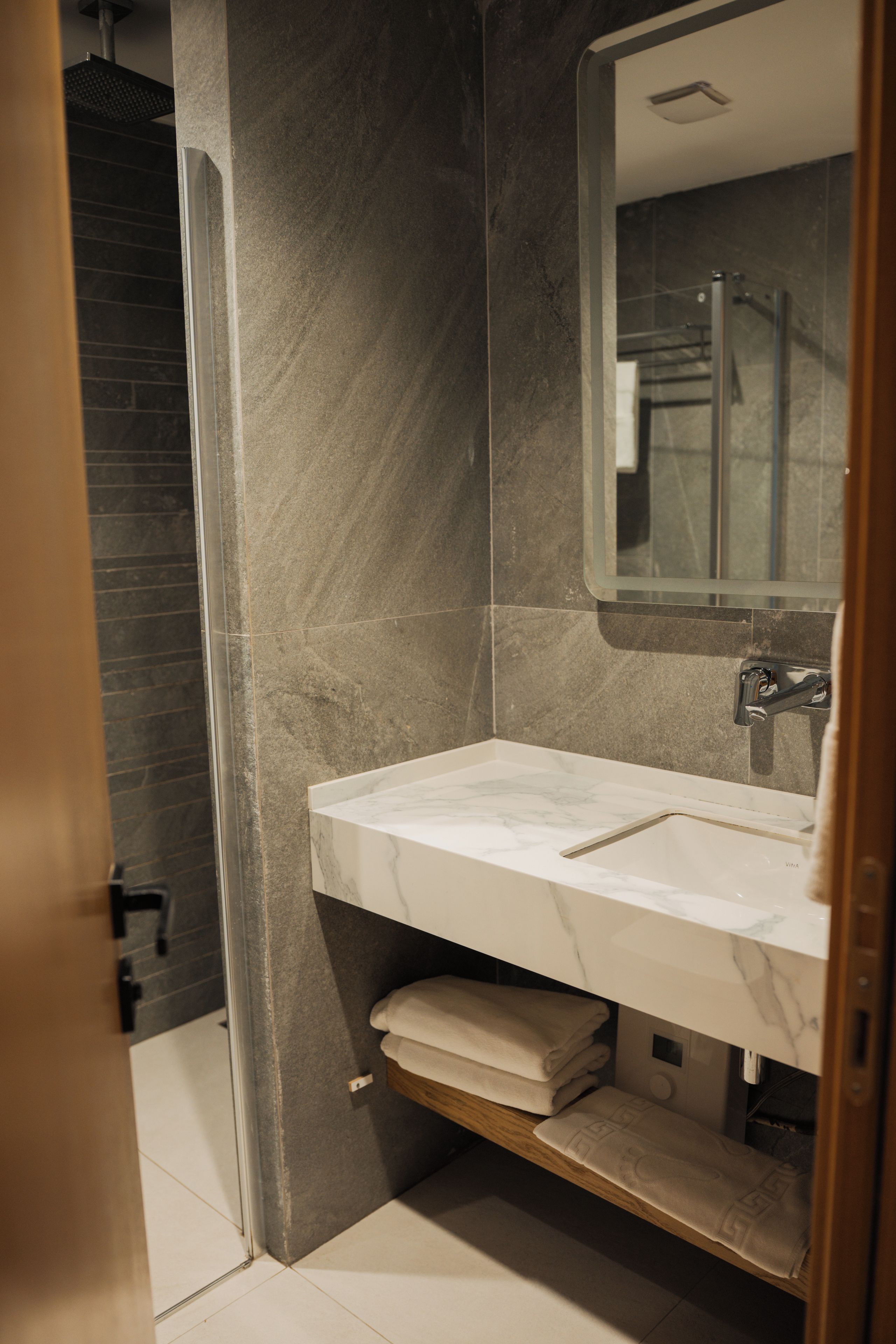 A modern bathroom with a marble sink, a mirror, and a shower area.