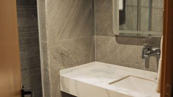 A modern bathroom with a marble sink, a mirror, and a shower area.