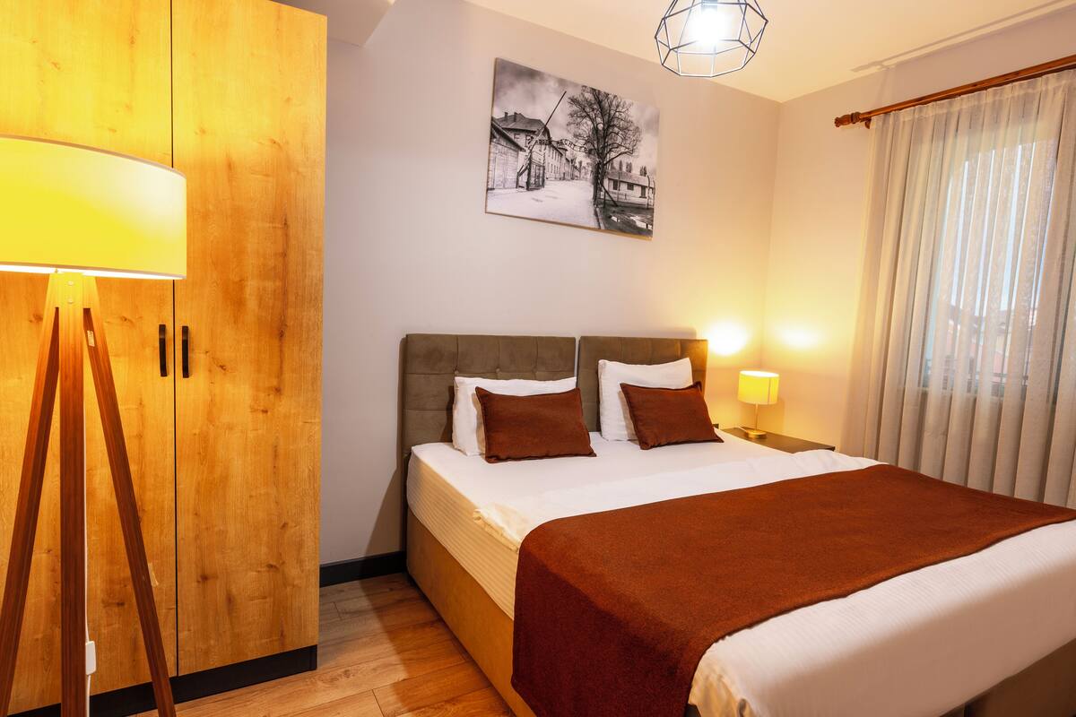 A hotel room with a bed, wooden wardrobe, and a painting on the wall.