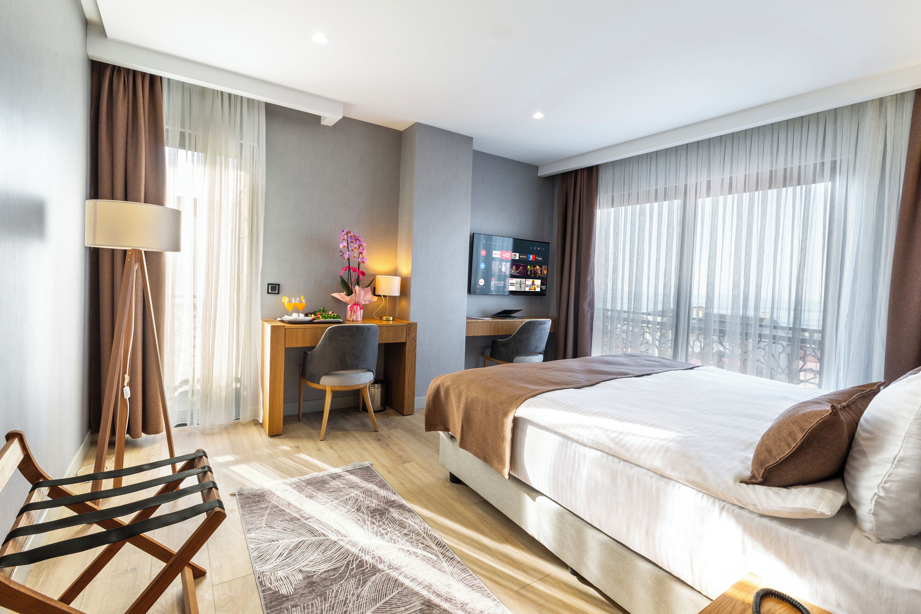 A hotel room with a bed, desk, chair, and a TV on the wall.