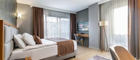 A modern hotel room with a bed, desk, chair, and a large window with curtains.