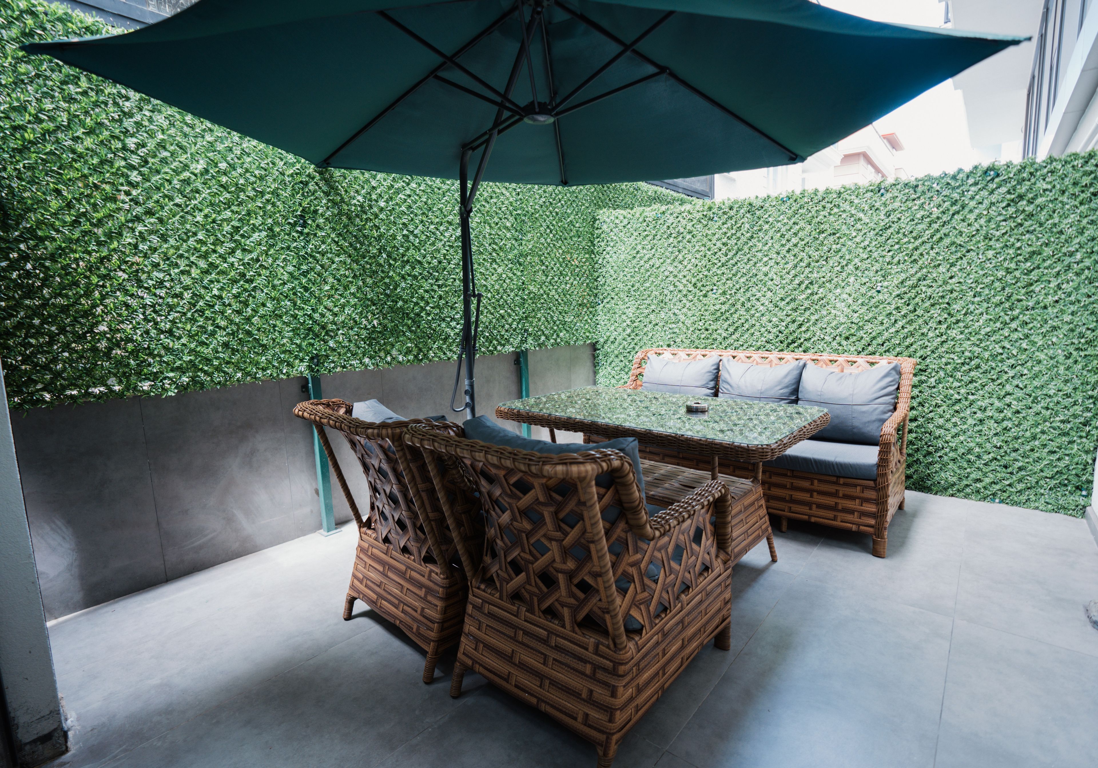 Área de pátio com móveis de vime, uma mesa e um guarda-sol.