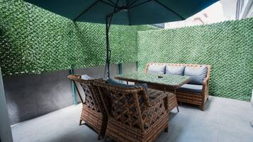 Área de pátio com móveis de vime, uma mesa e um guarda-sol.