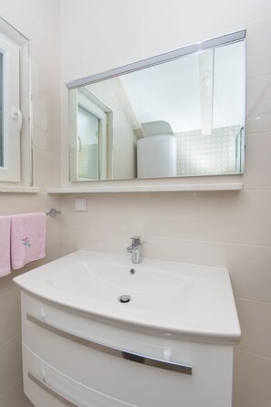 A bathroom with a white sink, a mirror above it, and a pink towel on the wall.