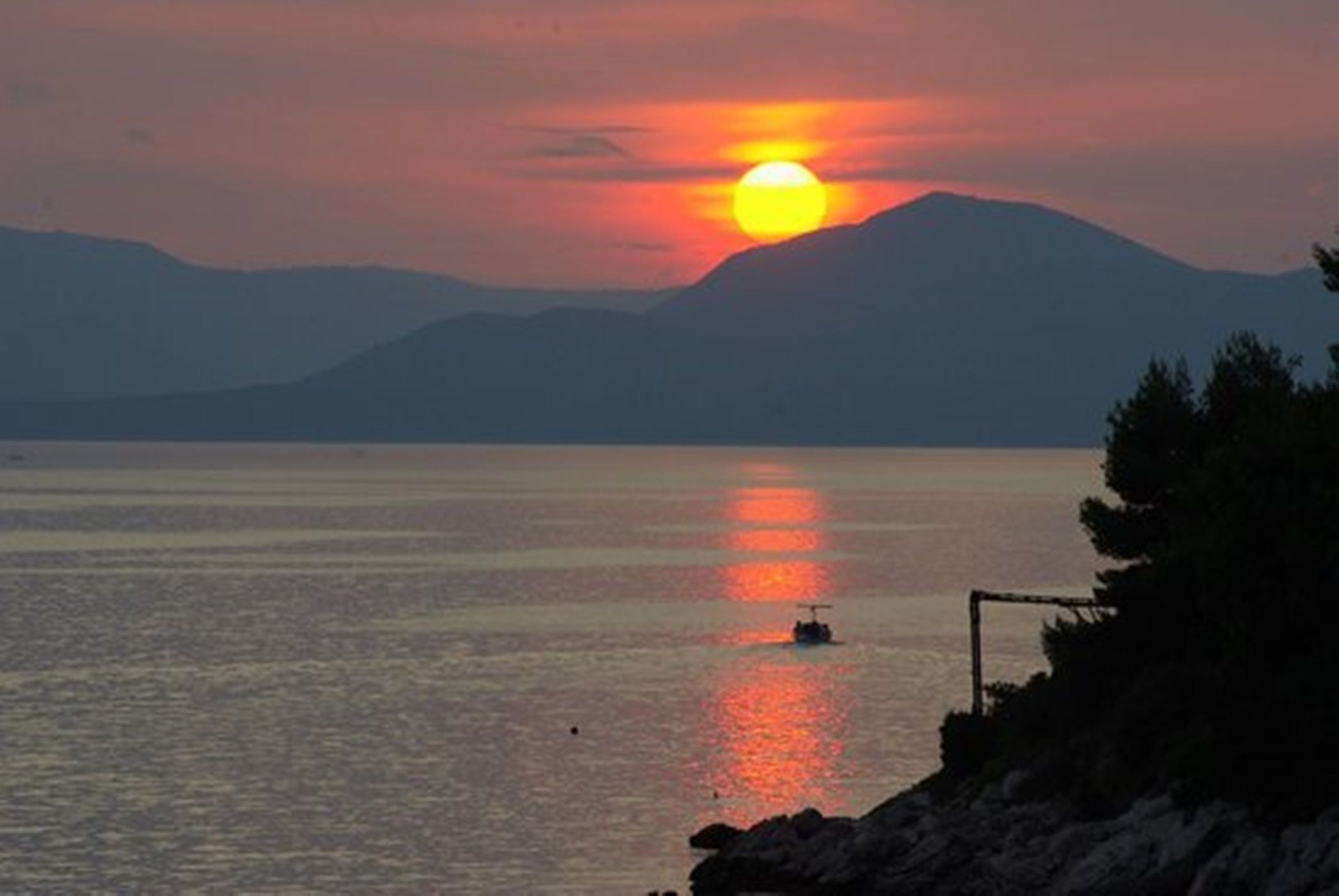 A sunset over a calm body of water with a boat and distant mountains.