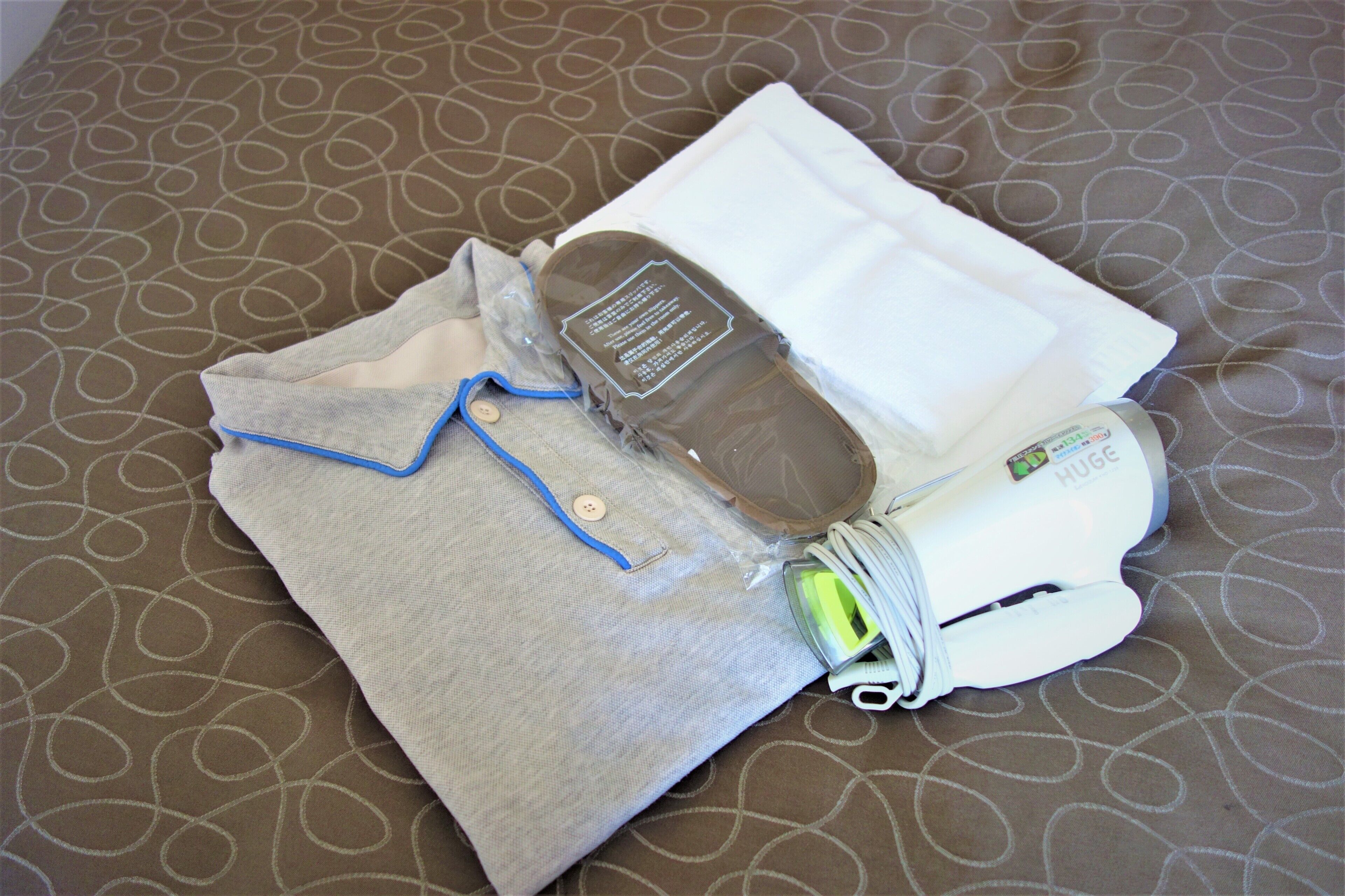 A neatly folded bedspread with a geometric pattern, a pillow, a folded shirt with a button, and a white device with a label.