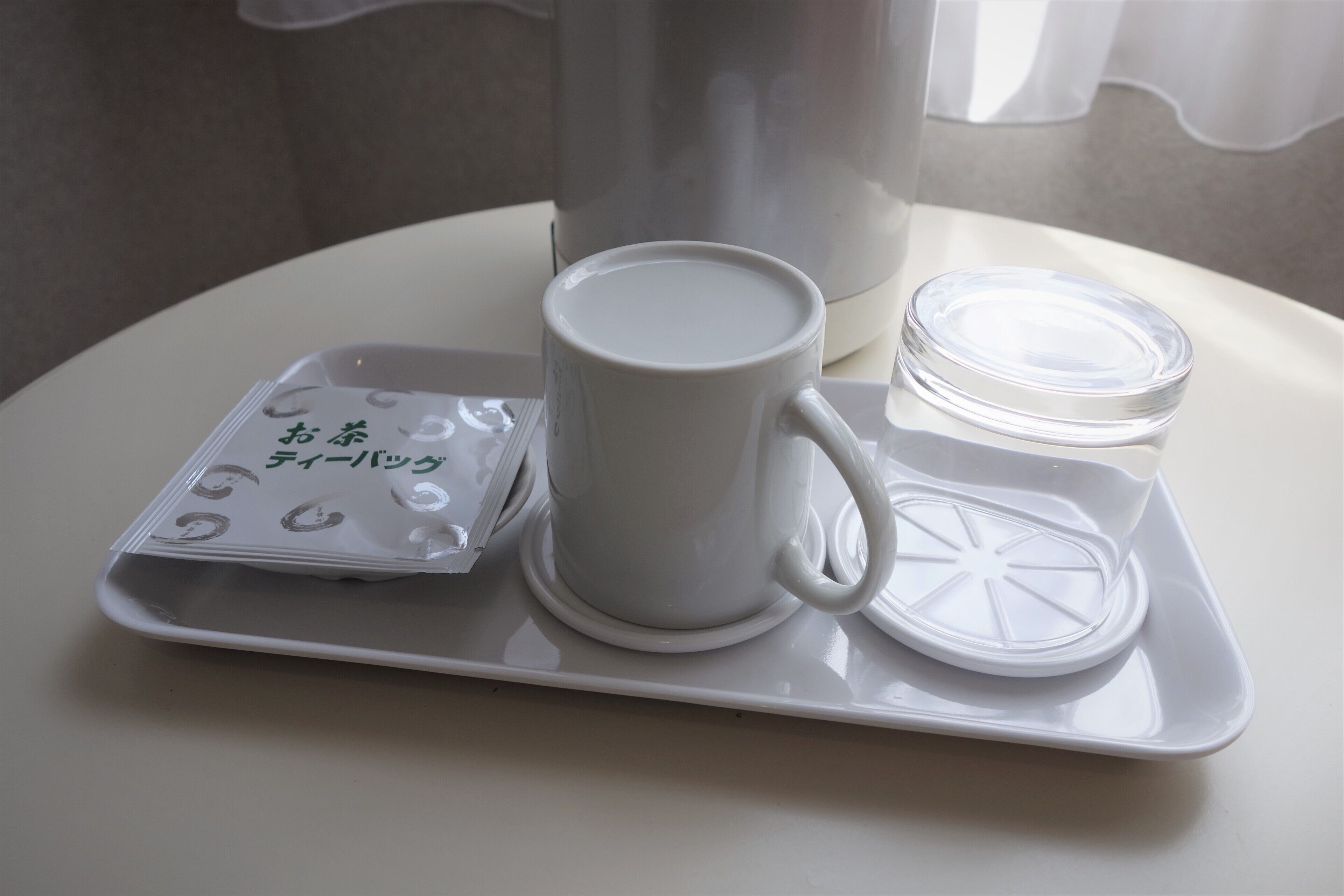 Ein weißes Tablett mit einer Tasse, einem kleinen Behälter und Teebeuteln auf einer weißen Oberfläche.