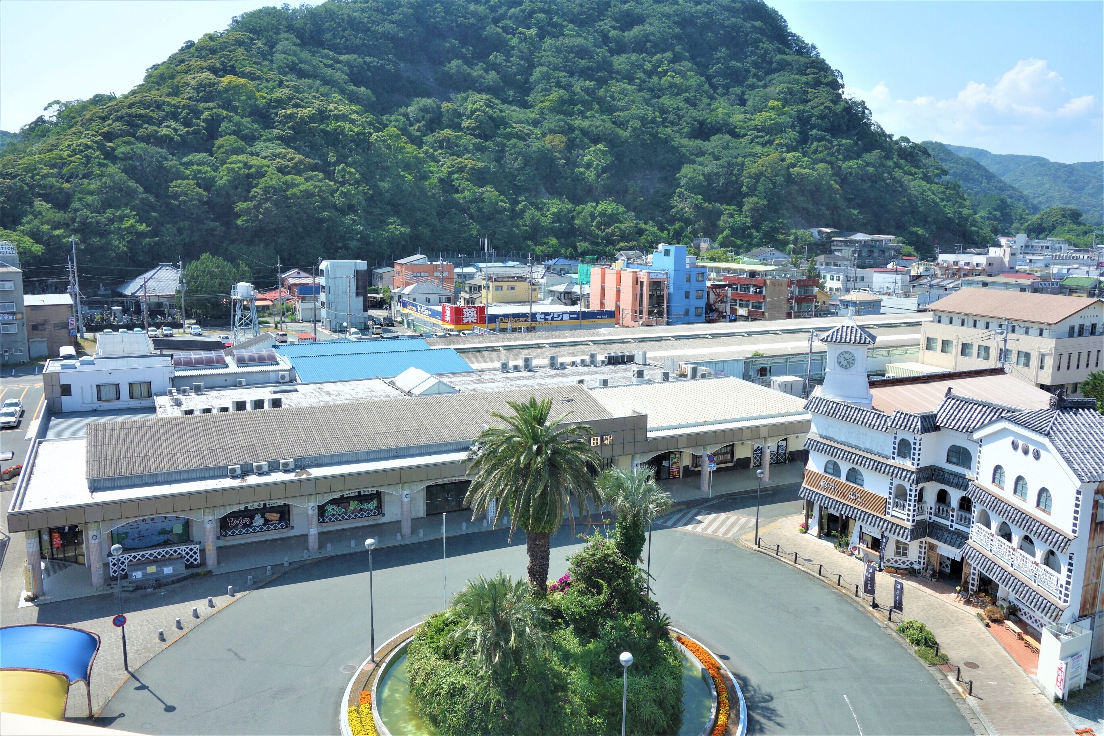 A town with a central roundabout, buildings with commercial signage, and a hill in the background.