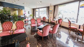 Un hall d’hôtel avec un sol en marbre, des fauteuils à revêtement rose, une table ronde et de grandes fenêtres offrant une vue panoramique.