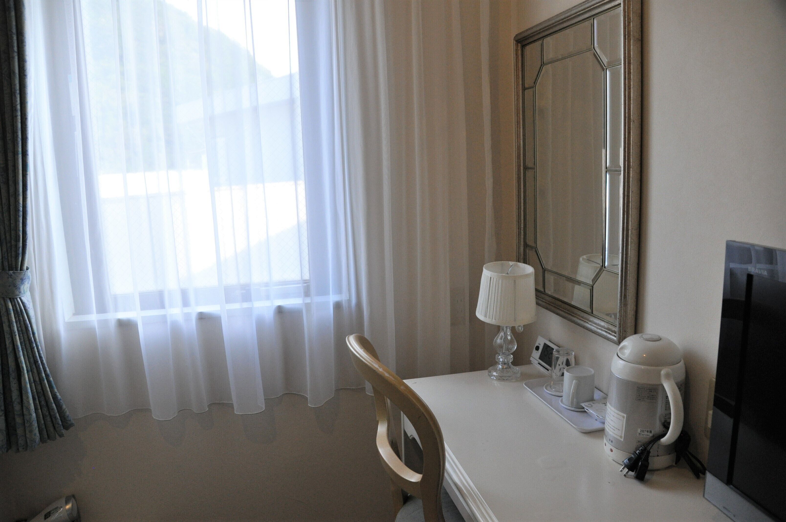 A hotel room with a bed, a desk with a lamp, a coffee maker, and a TV.